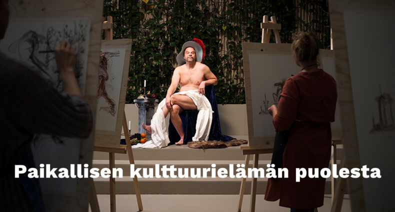 Alastonmallina oleva mies istuu tuolilla vyötäisillään valkoinen lakana.